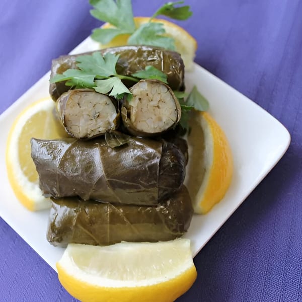 Dolmades, grape leaves stuffed with rice, garnished with parsley and lemon wedges on a white plate.