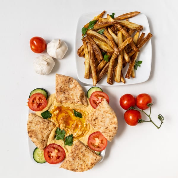 Hummus with pita bread, tomatoes, cucumbers, and a side of golden french fries.