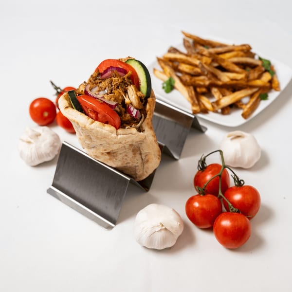 Chicken shawarma pita with tomatoes, onions, and cucumbers, served with fries, garlic, and cherry tomatoes.