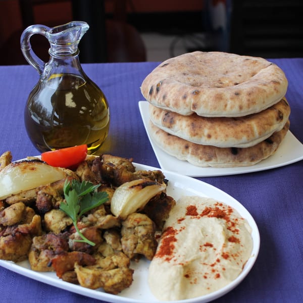 Middle-eastern chicken shawarma with hummus, pita bread, and olive oil on a purple tablecloth.