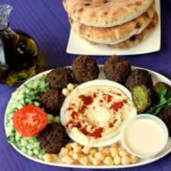 A platter of falafel, hummus, salad, chickpeas, and tahini sauce, with pita bread and olive oil.